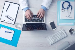 Group Health Insurance Health Doctor on laptop, stethoscope on top of patient files for Group Health Insurance.