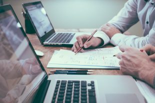 Business man and colleague reviewing document together with two laptops on desk and pen in hand for Professional Liability Insurance.